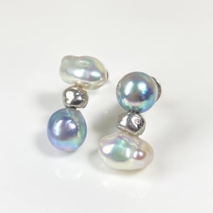 Könnte beinhalten: Ein Paar Perlenohrringe. Jeder Ohrring hat drei Perlen: eine große, schillernde, tropfenförmige Perle unten, eine kleine Silberperle in der Mitte und eine kleinere, runde Perle oben. Die Perlen haben einen glänzenden Glanz.