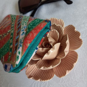 May include: A colorful patterned fabric pouch with a pink ceramic rose on a white background.