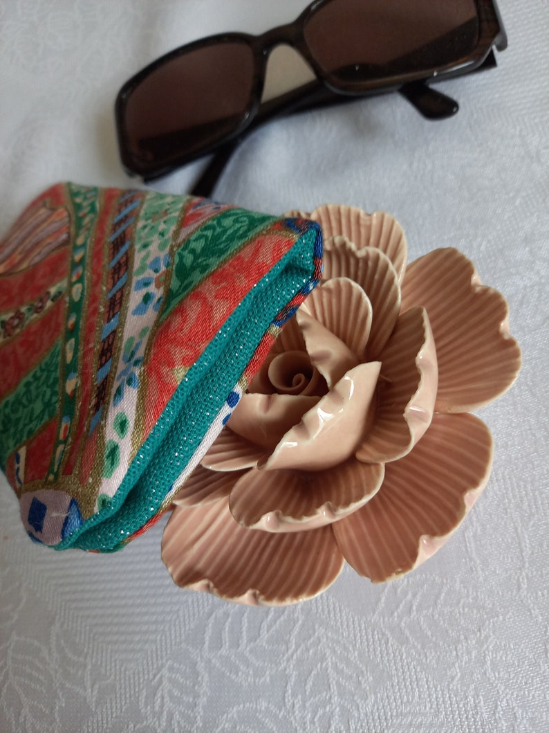 May include: A colorful patterned fabric pouch with a pink ceramic rose on a white background.
