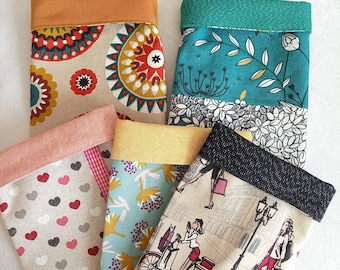 Puede incluir: Cinco bolsas de tela con diferentes patrones. Las bolsas están hechas de una tela de color claro con un ribete de color contrastante. Los patrones incluyen diseños geométricos, patrones florales y una escena de ciudad con una bicicleta.