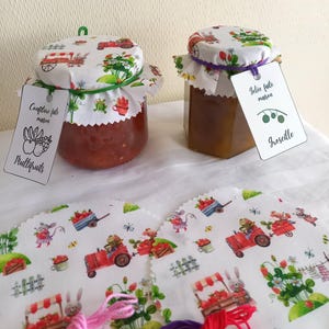 Peut inclure: Deux pots de confiture maison en verre avec des couvercles en tissu ornés d'un motif fantaisiste de fruits et légumes. Chaque pot a une étiquette avec du texte. En dessous, des morceaux de tissu avec des illustrations assorties et du fil à broder coloré.