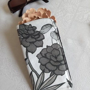May include: A white and black floral patterned glasses case with a zipper closure.