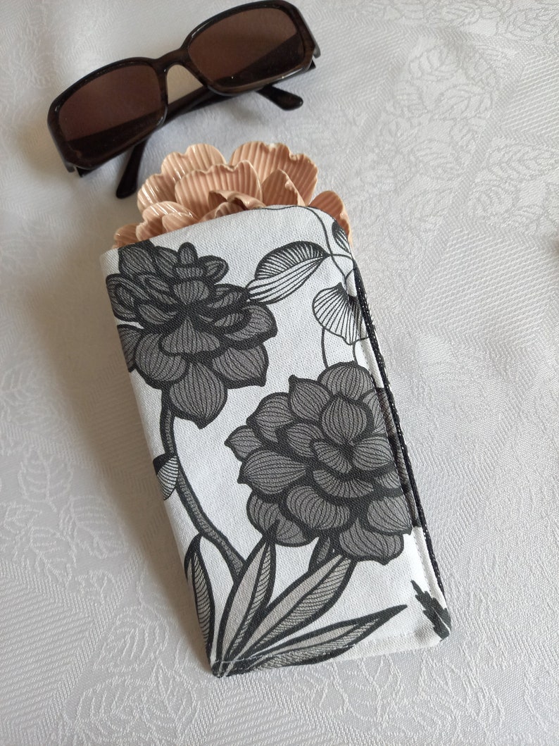 May include: A white and black floral patterned glasses case with a zipper closure.