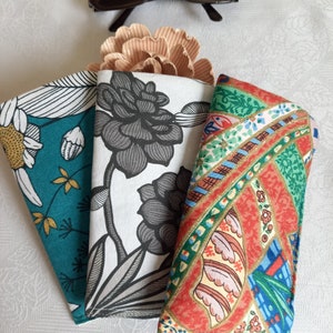 May include: Three fabric eyeglass cases with different patterns. The case on the left has a teal background with white and gold floral designs. The middle case has a white background with a black floral design. The case on the right has a red background with a colorful paisley design.