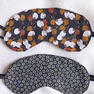 Puede incluir: Dos antifaces para dormir con bandas elásticas. Uno tiene un fondo gris oscuro con un estampado floral en blanco, naranja y rojo. El otro tiene un fondo azul marino con un pequeño patrón floral amarillo repetido.