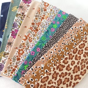 May include: A collection of eleven fabric headbands arranged in a fan shape, featuring various patterns including dark blue, green with leaf prints, floral designs in pink and orange, and several variations of leopard and cheetah animal prints.