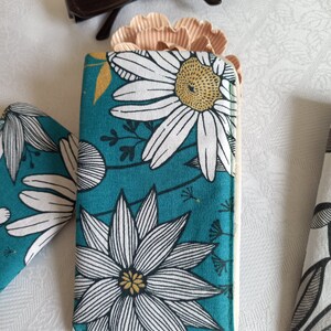 May include: A teal blue fabric glasses case with a white and black floral pattern. The flowers have yellow centers. The case is closed.