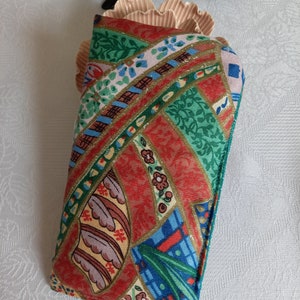May include: A red, green, blue, and gold patterned fabric eyeglass case. The case is made of a soft, quilted fabric and has a zipper closure.