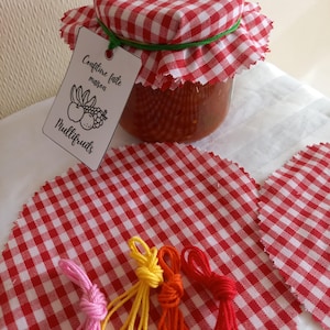 Könnte beinhalten: Ein Glas mit selbstgemachter Multifruchtmarmelade mit einem roten und weißen karierten Stoffdeckel. Das Glas ist mit "Confiture faite maison Multifruits" beschriftet. Es gibt vier Garnrollen in Pink, Gelb, Orange und Rot.
