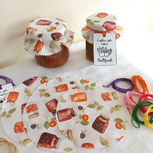 Può includere: Quattro cerchi di stoffa bianca con un motivo di vasetti di marmellata e bacche. I cerchi sono su una superficie bianca con un vasetto di marmellata con un coperchio di stoffa e un'etichetta che recita "Confiture faite maison Multifruits". Ci sono anche diversi rocchetti di filo colorato.