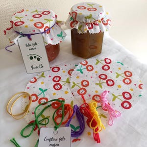 Peut inclure: Deux pots en verre de confitures faites maison avec des couvercles en tissu à motifs de cerises. Les pots sont étiquetés. De la ficelle colorée et des cercles de tissu à motifs de cerises sont également visibles.