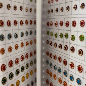 May include: A sheet of colorful, round, adhesive gems with gold trim. The gems are arranged in rows on a white background.