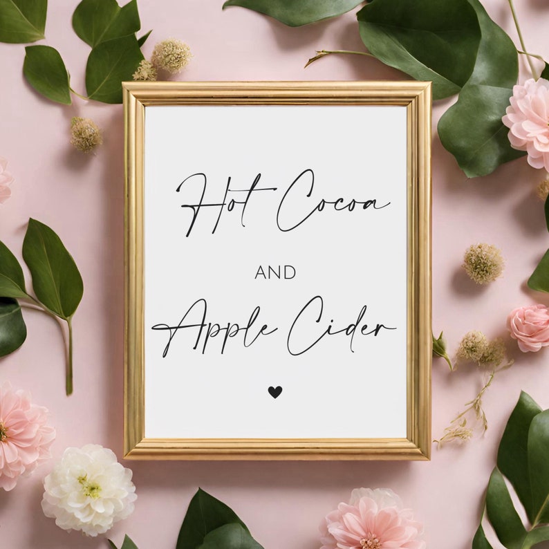 May include: A framed sign with gold trim displays the words "Hot Cocoa AND Apple Cider" in elegant black script, with a small black heart beneath. The sign is surrounded by pink flowers and green leaves on a pink background.