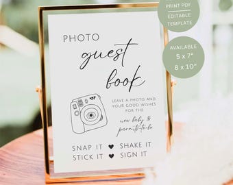 May include: A white sign in a gold frame with black text reading PHOTO guest book, LEAVE A PHOTO AND YOUR GOOD WISHES FOR THE new baby & parents-to-be, SNAP IT, SHAKE IT, STICK IT, SIGN IT, and an illustration of an instant camera.