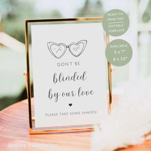 Op de afbeelding: Een ingelijst bord met een goudkleurig metalen frame. Het witte bord heeft een tekening van hartvormige zonnebrillen en de tekst "DON'T BE blinded by our love. PLEASE TAKE SOME SHADES!". Het bord is verkrijgbaar in formaten van 12,7 x 17,8 cm en 20,3 x 25,4 cm.