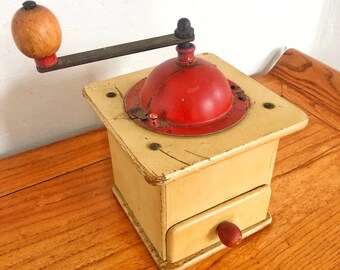 May include: A vintage wooden coffee grinder with a red metal top and a crank handle. The grinder has a drawer for collecting the ground coffee.