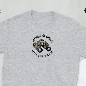 May include: A gray t-shirt with a black graphic of binoculars and the text "Afraid of girls, not the dark".