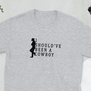 May include: A gray t-shirt with a black silhouette of a cowboy and the text "I SHOULD'VE BEEN A COWBOY".