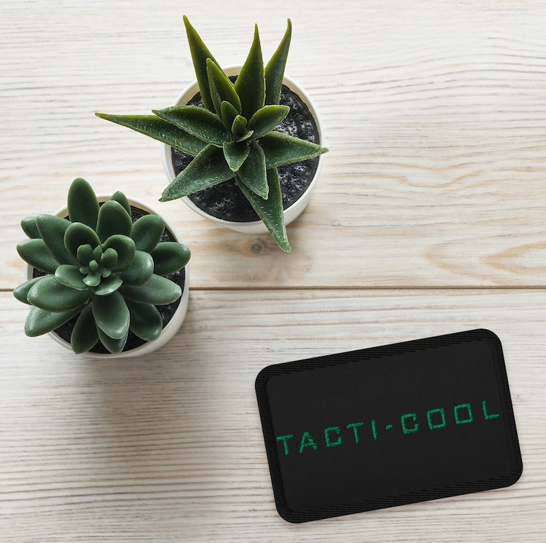 Peut inclure: Un patch noir avec le texte "TACTI-COOL" en lettres vertes. Deux succulentes en pot sont en arri&egrave;re-plan.
