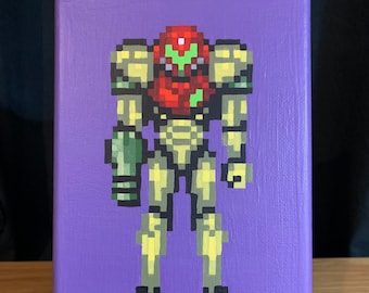 May include: A pixel art painting of a video game character on a purple canvas. The character is a yellow and green robot with a red helmet. The painting is on a small wooden easel.