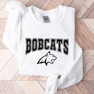 May include: White sweatshirt with black text that reads "BOBCATS" and a black silhouette of a bobcat.