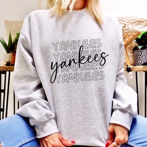 May include: A gray sweatshirt with a black graphic print of the word "Yankees" repeated in a stacked pattern.