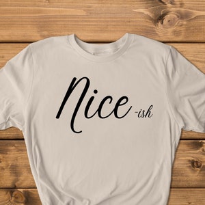 May include: A light beige t-shirt with the text "Nice -ish" printed in black cursive font.