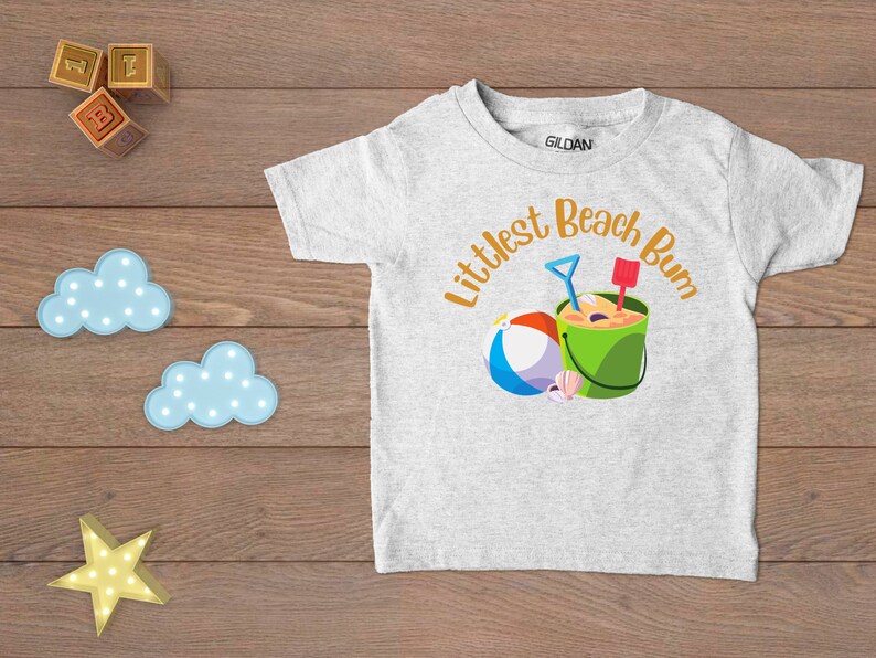 Littlest Beach Bum, featuring a beach ball and bucket of sand.  Shown on a white t-shirt.