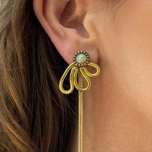 Op de afbeelding: Gouden oorhangers met een bloemvormig ontwerp en een groene opaalsteen in het midden.