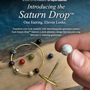 May include: Image of the Saturn Drop&trade; earring with interchangeable gemstone centers. The earring is gold-colored, with a circular design and a variety of colorful gemstones. The text reads "Introducing the Saturn Drop&trade; One Earring, Eleven Looks."