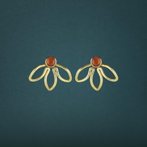 May include: A pair of gold-toned stud earrings featuring a central round orange stone set within a metal frame that extends into three open, petal-like loops. The design creates a symmetrical floral shape with a polished finish and smooth edges.