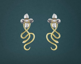 May include: A pair of drop earrings featuring a silver-toned flower top with a central white pearl accent. Below the flower, a gold-toned metal wire curves into a fluid, elongated, and swirling shape that extends downward from the floral element.