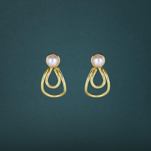 May include: A pair of gold-toned stud earrings featuring a round white pearl at the top, connected to a dangling open teardrop-shaped metal loop. The design consists of a smooth, polished gold finish that contrasts with the luster of the pearl.