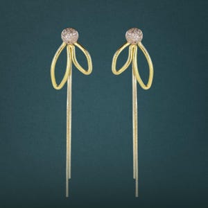 May include: A pair of gold-toned drop earrings featuring a spherical stud encrusted with small clear stones. Each earring has a looped wire design extending into a long, slender, flexible chain that hangs vertically from the base of the stud.