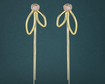Peut inclure: Une paire de boucles d'oreilles pendantes dorées avec un clou sphérique incrusté de petites pierres claires. Chaque boucle présente un design en fil bouclé se prolongeant par une longue chaîne fine et souple suspendue verticalement.