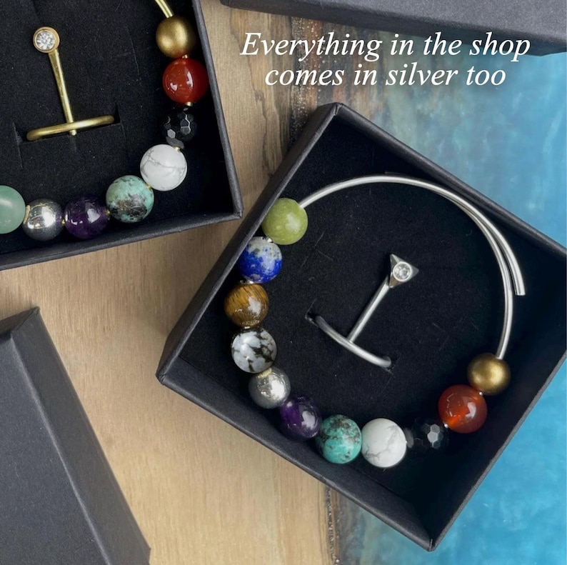 May include: Jewelry set in black boxes. One set features a gold-toned ring with a small crystal and a bracelet with colorful beads. The other set includes a silver-toned ring with a crystal and a bracelet with colorful beads. Text on the image says "Everything in the shop comes in silver too."