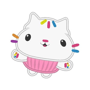 Könnte beinhalten: Eine weiße Katze mit einem rosa Cupcake-förmigen Rock und bunten Streuseln auf dem Kopf. Die Katze hat schwarze Augen und eine rosa Nase.