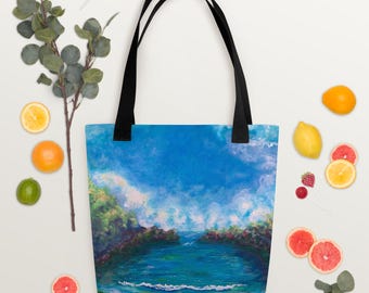 Puede incluir: Bolso tote con una pintura de paisaje de cielo azul, mar y árboles verdes. El bolso tiene asas negras. La imagen está rodeada de fruta y un caramelo.