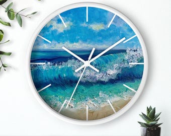 Può includere: Orologio da parete rotondo bianco con un'onda oceanica blu e schiuma bianca che si infrange su una spiaggia sabbiosa. Il quadrante dell'orologio ha lancette bianche e numeri neri.