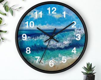 Può includere: Un orologio da parete con cornice nera con un design a onda oceanica blu e bianca. Il quadrante dell'orologio ha numeri bianchi e lancette nere.
