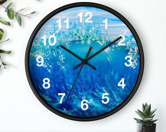 Può includere: Un orologio da parete con cornice nera e un design astratto di onda blu e bianca. Il quadrante dell'orologio ha numeri bianchi e lancette nere.