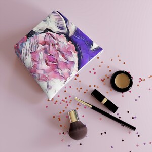 Puede incluir: Un neceser con estampado floral con un diseño de flores rosas y moradas. La bolsa está rodeada de artículos de maquillaje, incluyendo un pincel, lápiz labial y sombra de ojos, sobre una superficie rosa. Confeti disperso añade un toque decorativo.