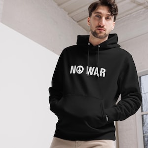 Könnte beinhalten: Schwarzer Kapuzenpullover mit dem weißen Schriftzug "NO WAR" und einem Friedenssymbol. Der Hoodie hat eine Vordertasche und eine Kapuze mit Kordelzug. Das Design ist schlicht und kühn und vermittelt eine Botschaft des Friedens.