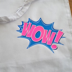 K&ouml;nnte beinhalten: Wei&szlig;e Stofftasche mit einem Comic-artigen Grafikdruck in Blau und Pink, der "WOW!" sagt.