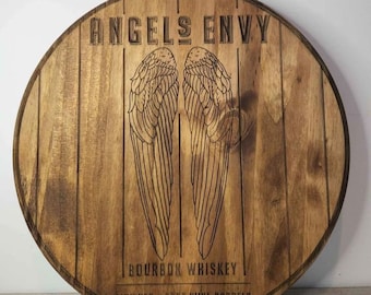 May include: A round wooden sign with the text "Angels Envy Bourbon Whiskey Finished in Port Wine Barrels" and a pair of angel wings.