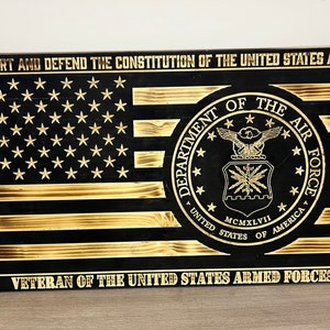 Puede incluir: Un letrero de madera con fondo negro y letras doradas. El letrero presenta una bandera estadounidense con un patrón de estrellas doradas, el sello del Departamento de la Fuerza Aérea y el texto "SUPPORT AND DEFEND THE CONSTITUTION OF THE UNITED STATES AGAINST ALL ENEMIES, FOREIGN AND DOMESTIC I DO SOLEMNLY SWEAR THAT I WILL VETERAN OF THE UNITED STATES ARMED FORCES".