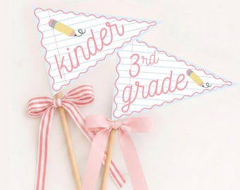 Op de afbeelding: Twee driehoekige wimpels op houten stokjes, de ene met het opschrift "kinder" en de andere met "3rd grade" in roze schrift. Beide hebben een witte achtergrond van gelinieerd papier, een gele potloodafbeelding en een geschulpte rand.