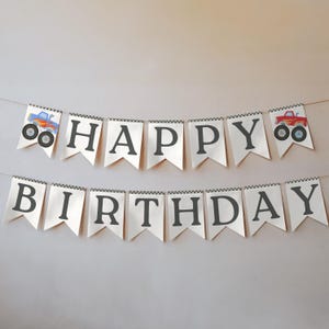 May include: A banner with the words "HAPPY BIRTHDAY" in dark gray letters. The banner is made of white pennants with a black and white checkered border. Two pennants feature monster truck illustrations in blue and red.