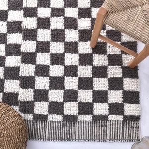 May include: A black and white checkered rug with a woven texture. The rug is on a white surface with two woven round stools.