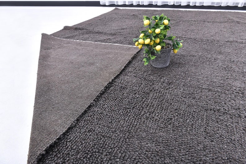 May include: A dark gray area rug with a textured surface. A small potted plant with yellow lemons is in the upper right corner of the rug.